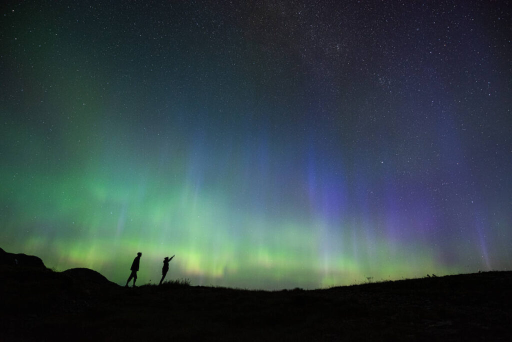 Aurora/Northern Lights overhead with two people watching and pointing to the sky, British Columbia.